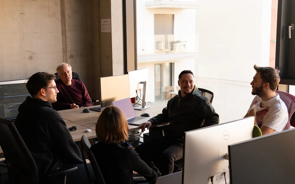 Rapid7 staff in discussion around a shared desk with monitors in a Rapid7 office