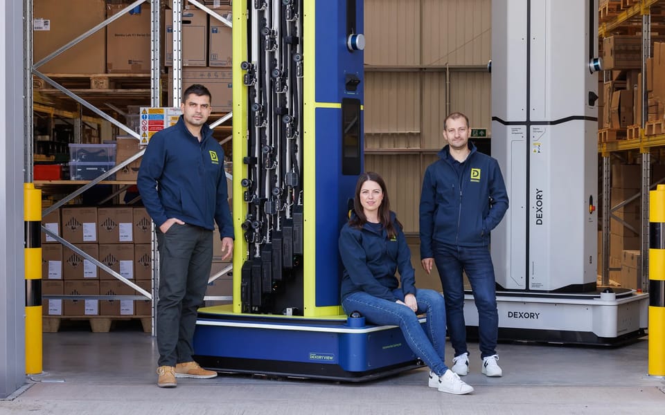 Dexory’s founders with two of the company’s autonomous warehouse scanning robots