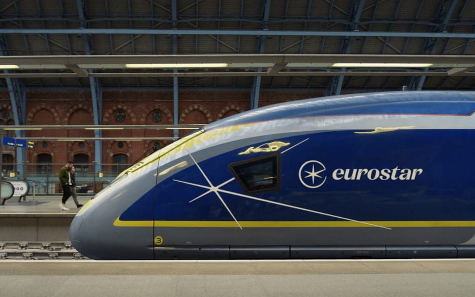 The nose of a blue and yellow Eurostar e320 train at a platform under the Victorian roof of London St Pancras International
