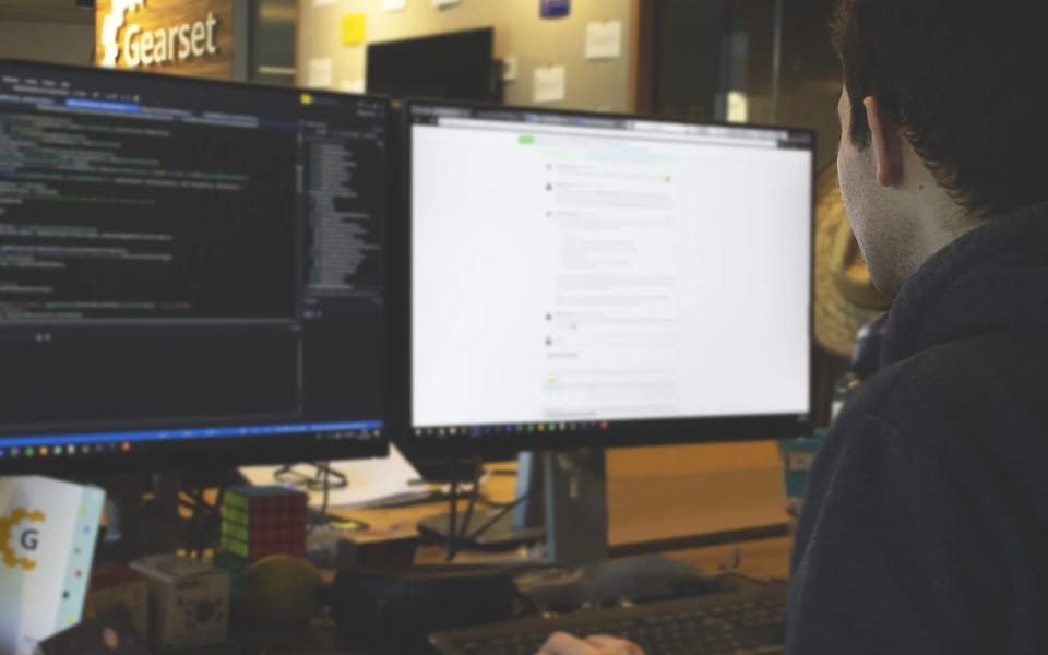 A Gearset employee working at two monitors, with the Gearset sign on the office wall behind
