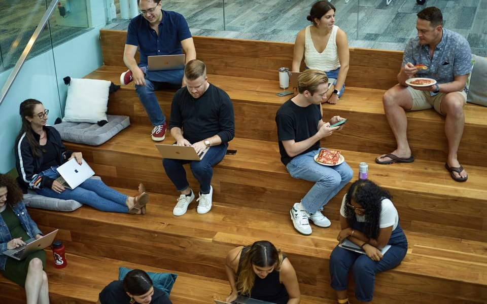 Braze employees working on laptops on wooden stepped seating in a Braze office