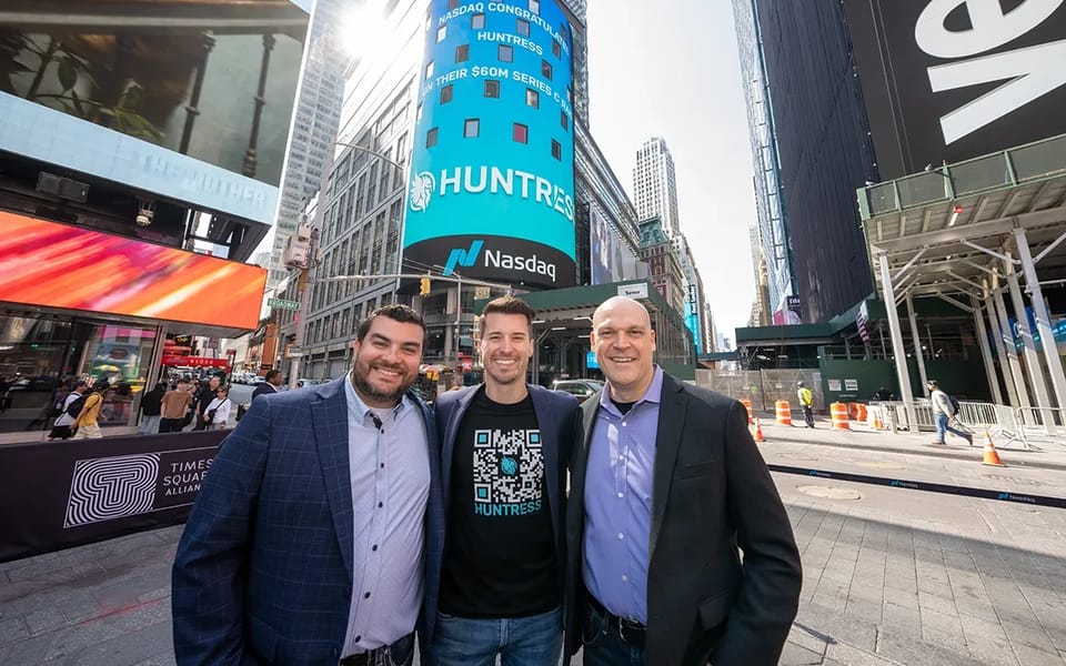 Members of the Huntress team in Times Square, New York, beneath a Nasdaq screen showing the Huntress name