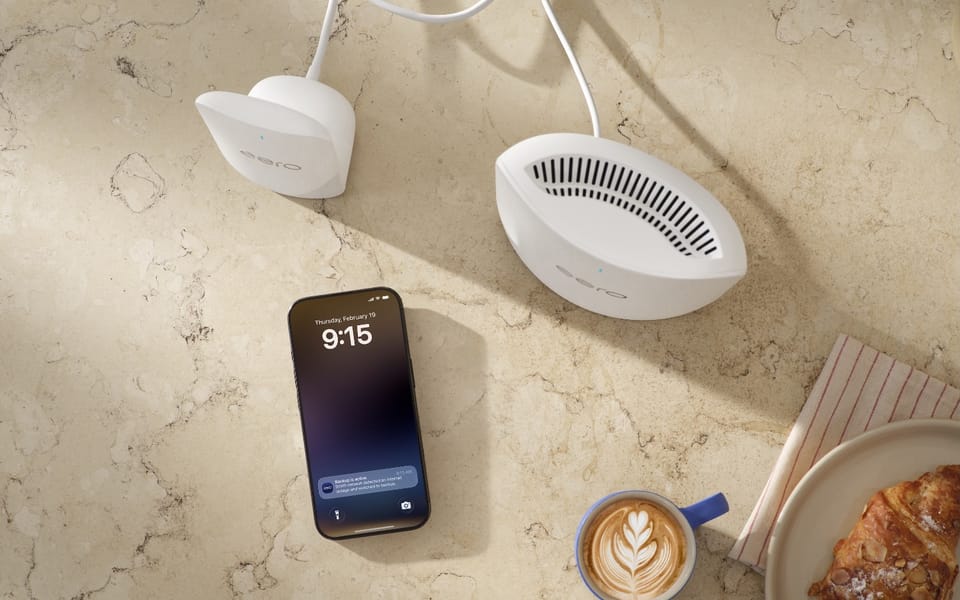 Two eero mesh Wi-Fi units on a counter beside a phone, a coffee and a croissant