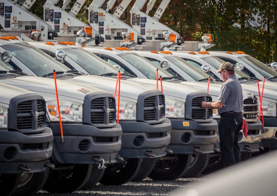 A row of white utility bucket trucks lined up for auction, with a buyer inspecting one