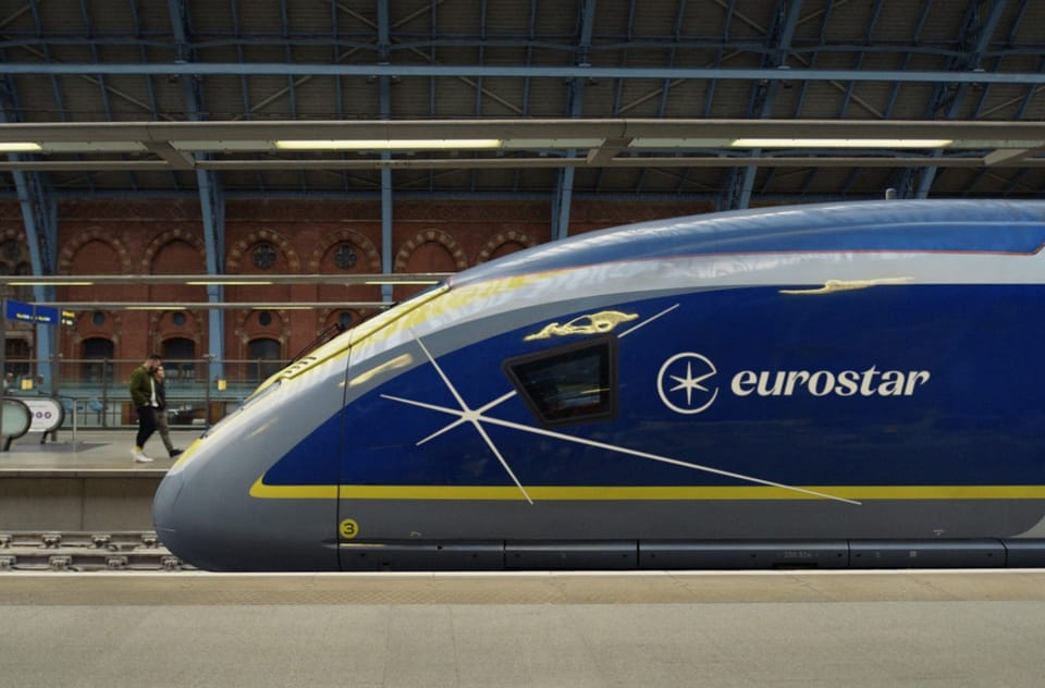 The nose of a blue and yellow Eurostar e320 train at a platform under the Victorian roof of London St Pancras International