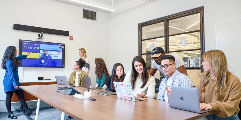 A manager presents to a team working on laptops in a monday.com office meeting room