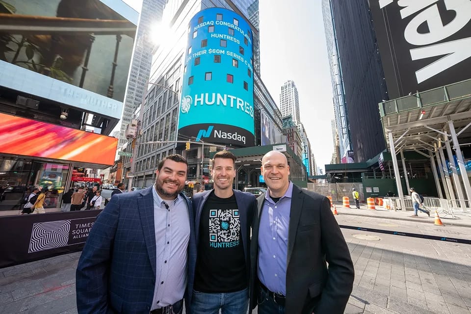Members of the Huntress team in Times Square, New York, beneath a Nasdaq screen showing the Huntress name
