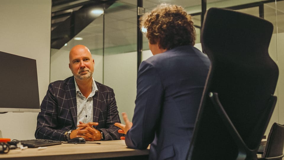 Two people in conversation across a desk in an office